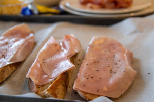 Toasted bread slices on a baking sheet with ham on top