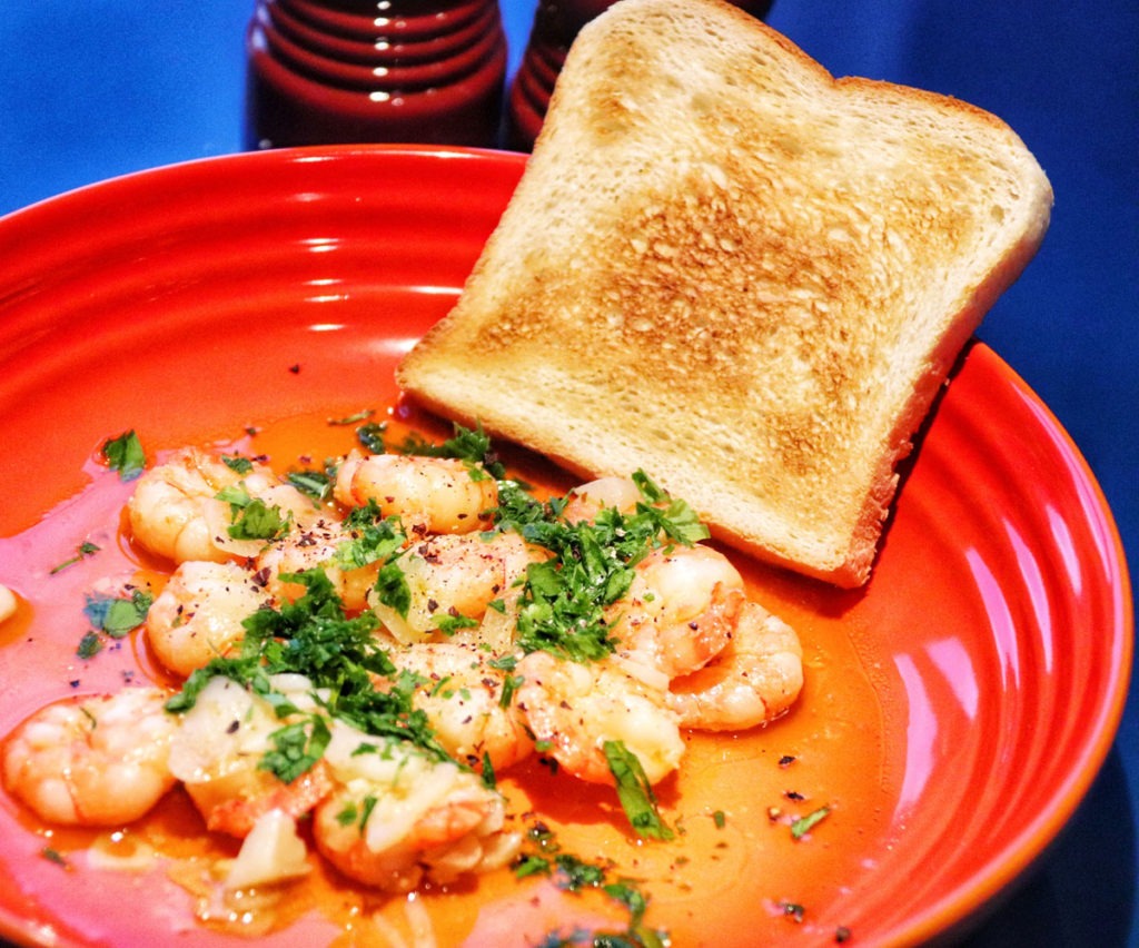 Sauteed garlic shrimps with toast on a orange stoneware pasta bowl