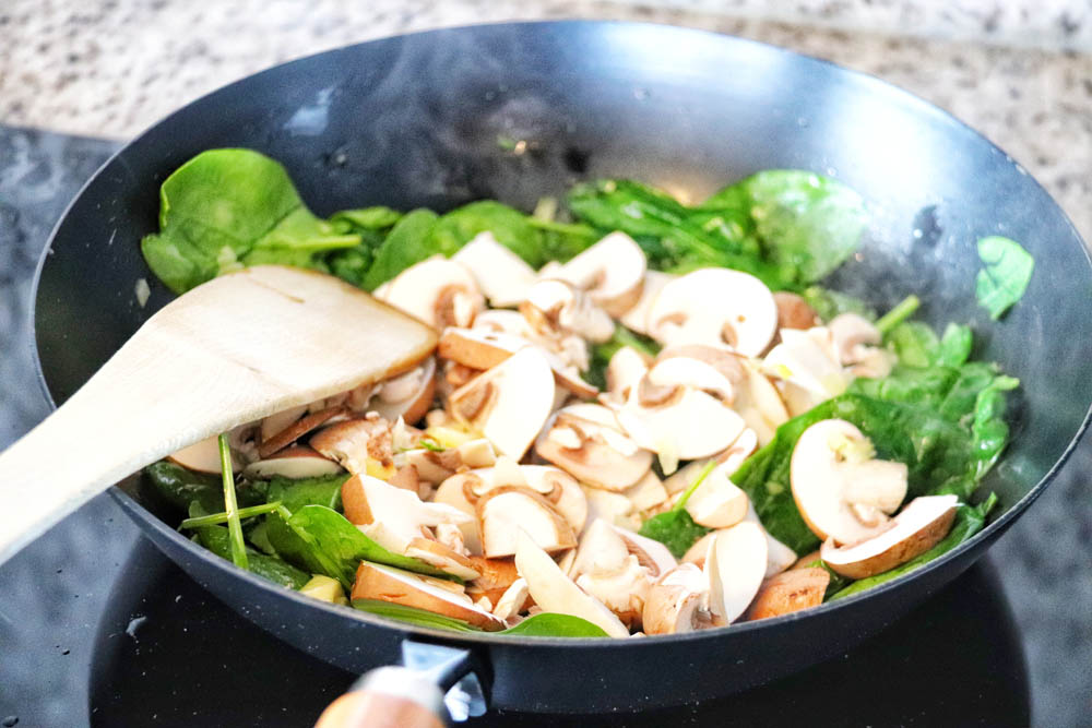 Spinach and mushrooms being sauteed in a frying pan
